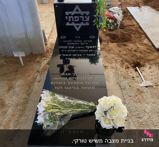 מצבה שחורה עם כיתוב בעברית ופרחים לבנים